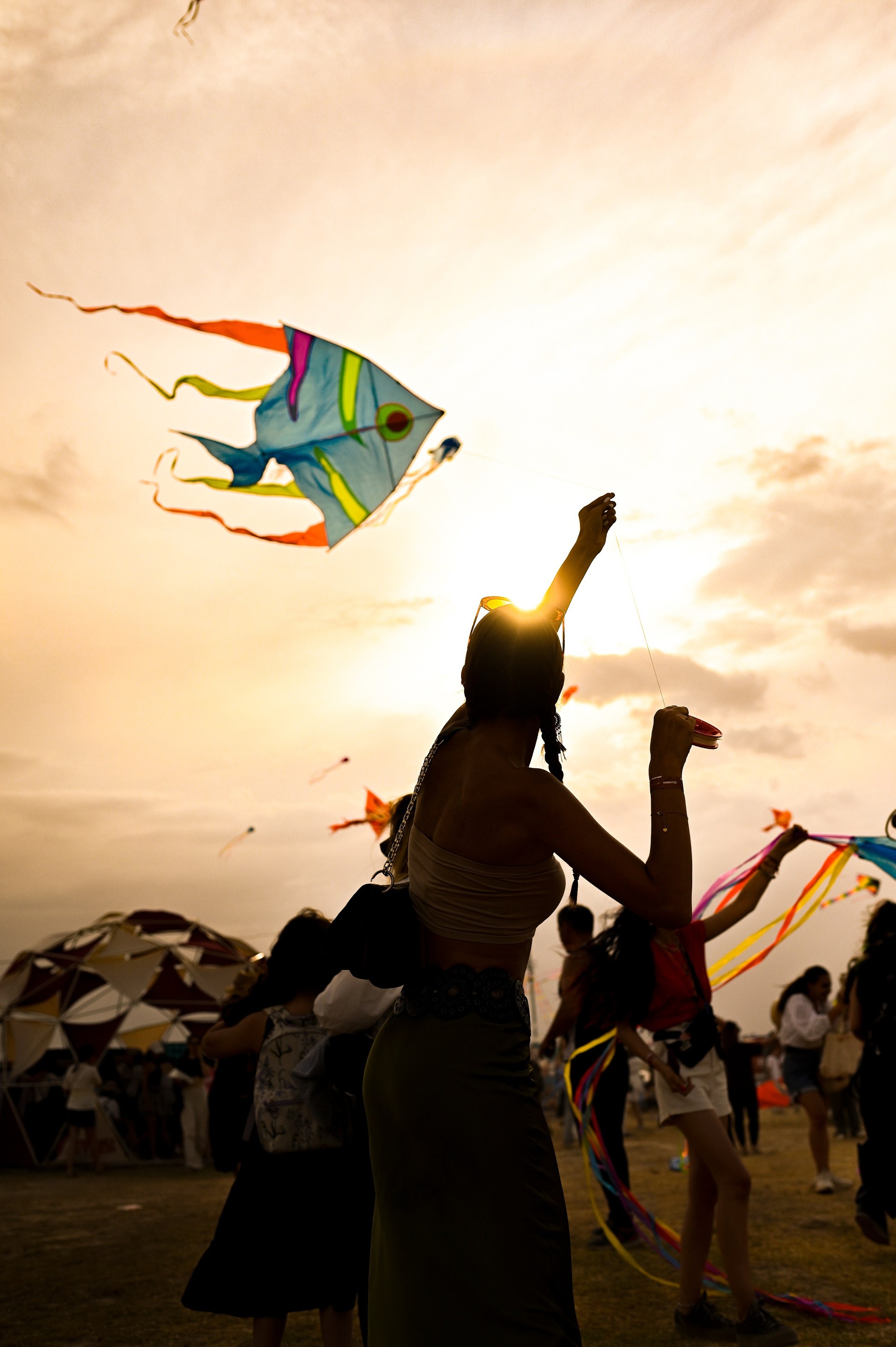 Festival-goer flying a fish-shaped kite at sunset