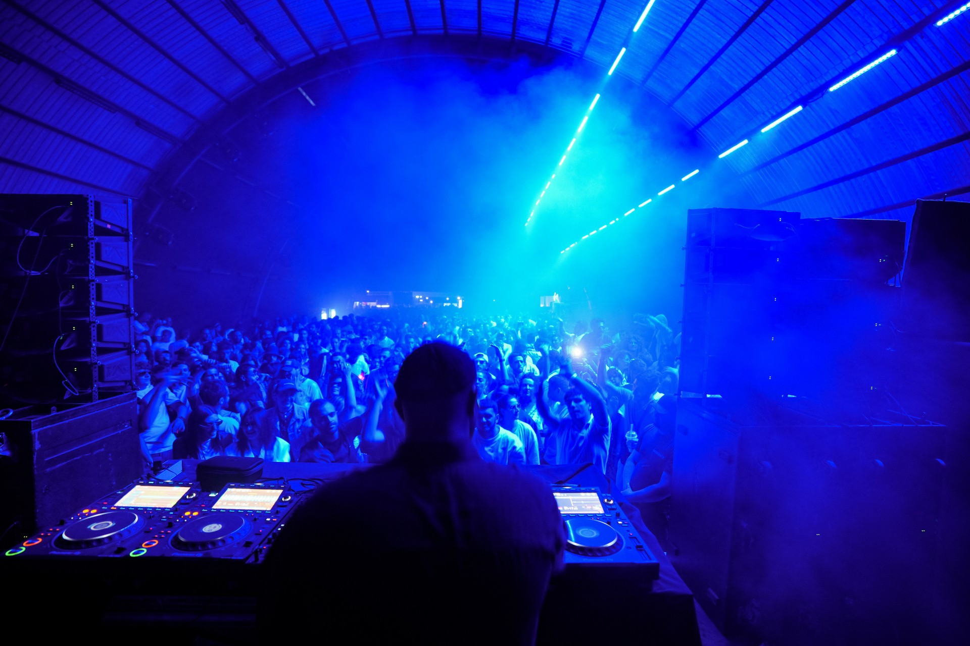 Blue-lit laser tunnel with the crowd facing the DJ booth